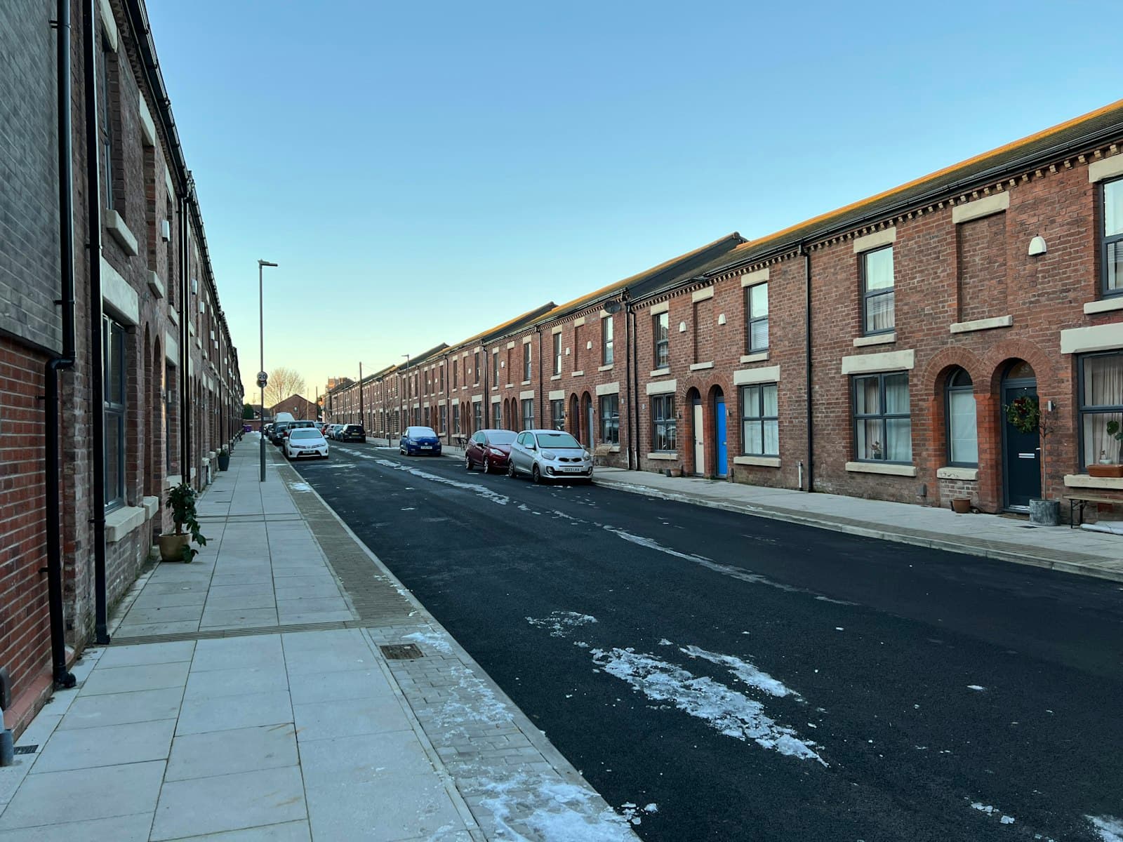 A street of brick terraced houses with cars parked outside